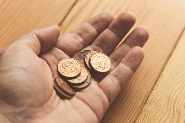 High angle shot of a person holding some coins over a wooden surface - Фото, изображение