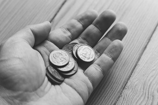 Grey scale high angle shot of a person holding some coins on wooden surface - 写真・画像