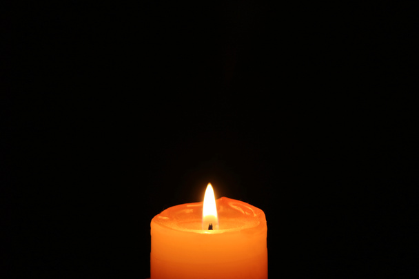 eine orangefarbene Kerze, die in der Dunkelheit leuchtet, mit freiem Raum für Text oder Design - Foto, Bild