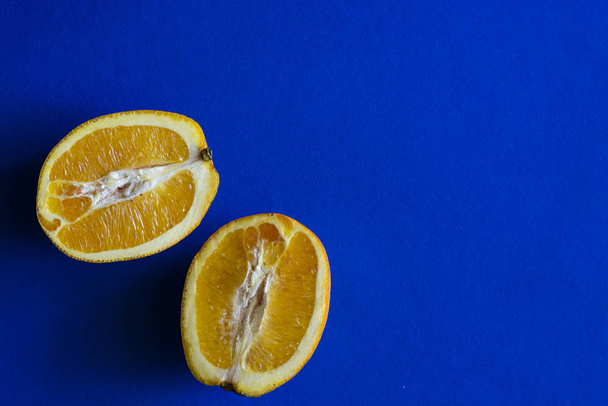 2 pieces of cut orange on blue background, minimalist photograph - Fotoğraf, Görsel
