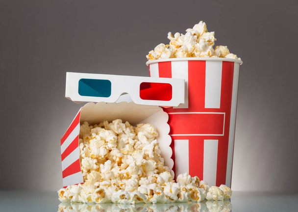 Two striped popcorn boxes, 3D glasses and popcorn spilled on gray. - Foto, afbeelding