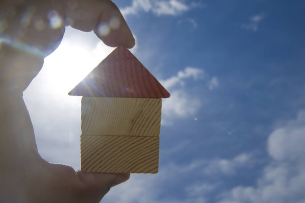  hand holding  wooden house toy against sunny sky with sun rays - Photo, Image