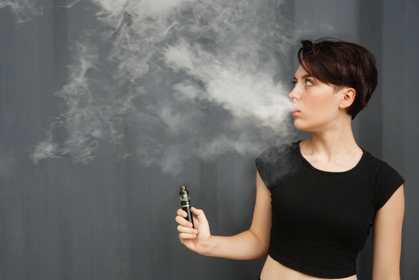 young girl smokes electronic cigarette. female model vaping a va - Foto, afbeelding