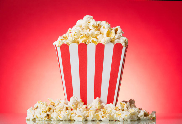Popcorn in large square box and around on bright red. - Φωτογραφία, εικόνα