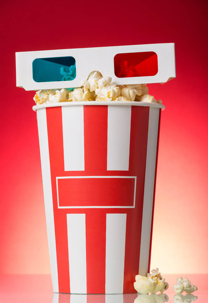 3D glasses, box popcorn and few nearby on bright red. - Foto, afbeelding