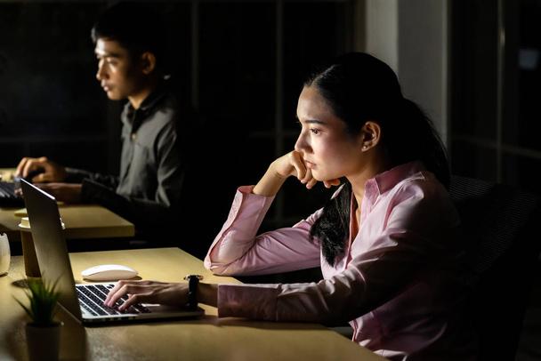 Young adult Asian businessman and woman working late at night in their office with desktop computer and laptop. Using as hard working and working late concept. - Foto, imagen
