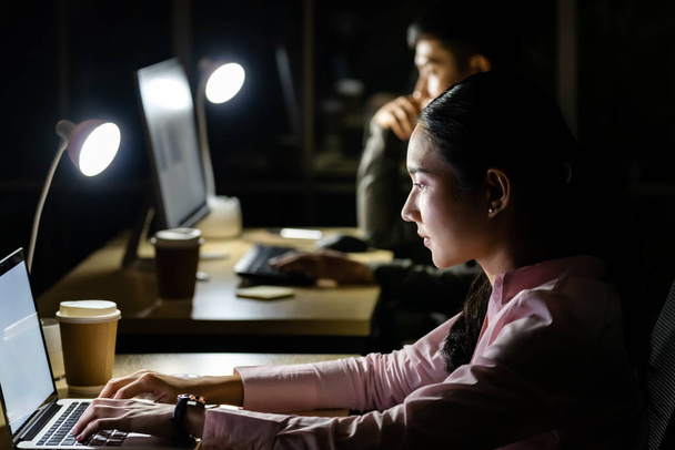 Young adult Asian businessman and woman working late at night in their office with desktop computer and laptop. Using as hard working and working late concept. - Photo, Image
