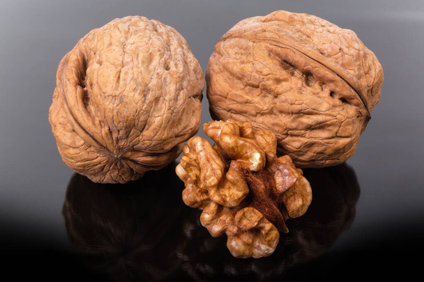 Celé vlašské ořechy a ořechové jádro na tmavém reflexním povrchu - Fotografie, Obrázek