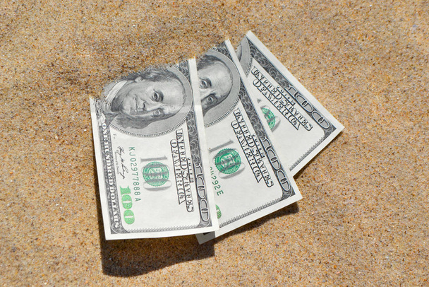 Pénz dolárok félig fedett homok fekszik a strandon közelkép. - Fotó, kép