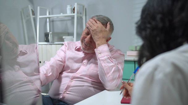 Mann sitzt im Krankenhauskabinett und hört auf Anweisungen der Ärzte  - Foto, Bild