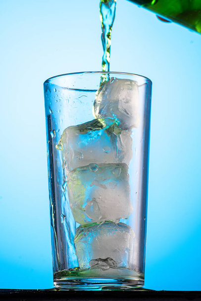geelgroene of koolzuurhoudende limonade in een glas met ijs, stroming en plons - Foto, afbeelding