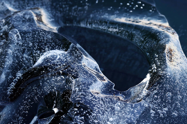 Кусок льда с замороженными пузырьками в воде. Маленький айсберг в воде
 - Фото, изображение