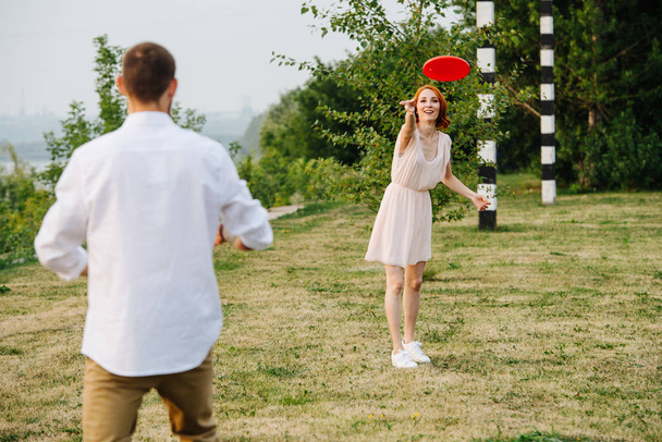 Man and woman playing frisbee in a park next to a river and forest ridge - Фото, изображение