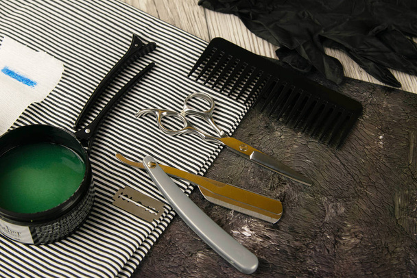 Narzędzia układające dla fryzjera, nożyczki, niebezpieczna żyletka, ostrze, rosa i zielony żel do włosów na pięknym ręczniku w paski - Zdjęcie, obraz