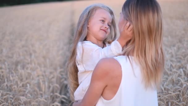 A young mother holds her little daughter in her arms and hugs her in a wheat field. - Footage, Video