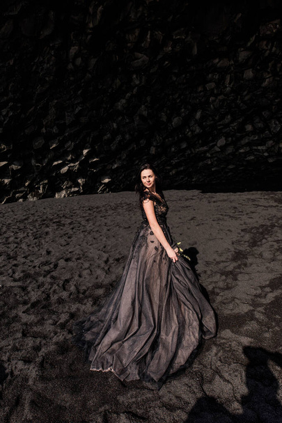 piękna i uśmiechnięta kobieta pozująca w jaskini z czarnym piaskiem z kwiatem kwiatów - Zdjęcie, obraz