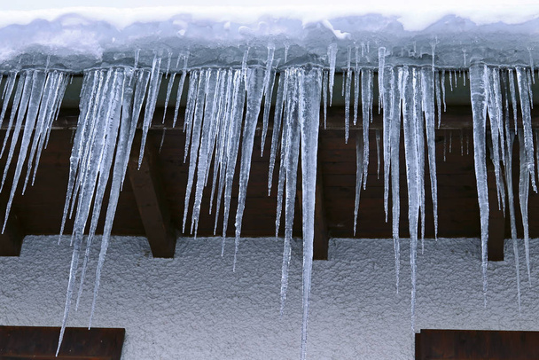 I ghiaccioli grandi pendono da un tetto di casa. Grandi ghiaccioli pericolosi su una casa - Foto, immagini