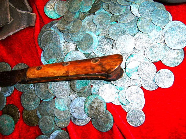 reconstruction d'un trésor à partir d'un placard de pièces d'argent du XVIIe siècle et d'un couteau sur fond rouge
 - Photo, image