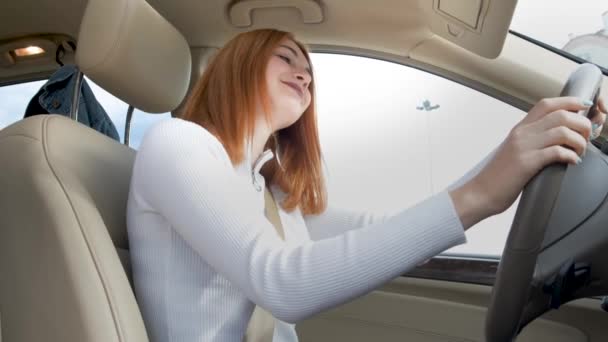 jonge vrouw bestuurder hebben plezier achter het stuur luisteren naar muziek in een auto. - Video