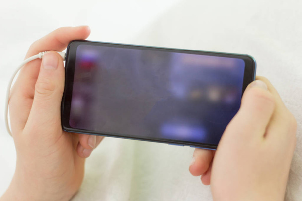 Een tiener houdt een smartphone vast met een wazige achtergrond. - Foto, afbeelding