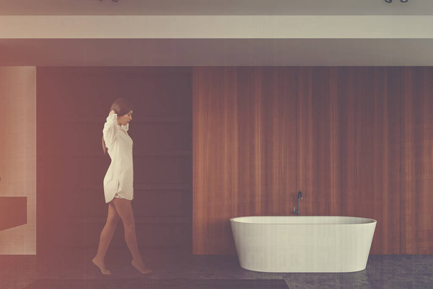 Woman walking in wooden bathroom with shelves - 写真・画像