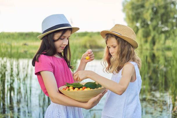 Two girls eating yellow cherries, summer day in nature - Фото, зображення