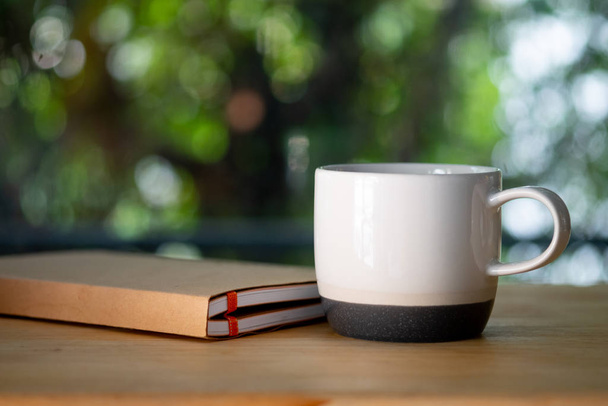 Белая керамическая чашка и книга на белом столе
 - Фото, изображение