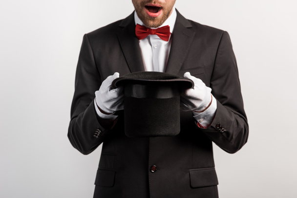 cropped view of shocked magician holding hat, isolated on grey - Photo, Image