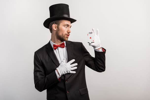 šokovaný kouzelník při pohledu na hrací karty, izolované na šedé - Fotografie, Obrázek