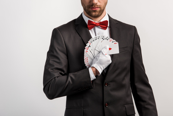 bijgesneden weergave van een bebaarde goochelaar die speelkaarten vasthoudt, geïsoleerd op grijs - Foto, afbeelding
