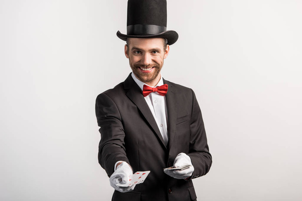 cheerful magician holding playing cards, isolated on grey - Photo, Image