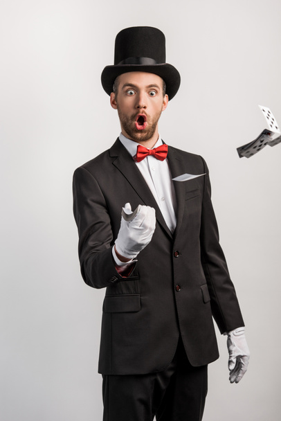 shocked magician with open mouth throwing playing cards, isolated on grey - Foto, afbeelding