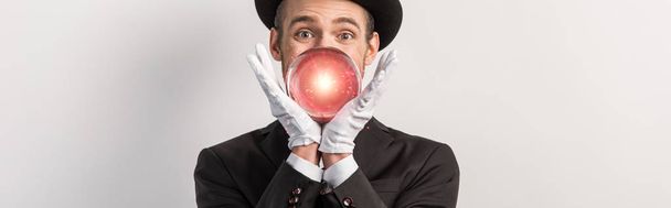 πανοραμική λήψη του συναισθηματικού μάγου κρατώντας κόκκινη μαγική μπάλα, απομονωμένη σε γκρι - Φωτογραφία, εικόνα