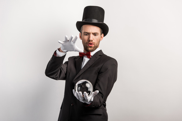 soustředěný profesionální kouzelník držící magickou kouli, izolovaný na šedi - Fotografie, Obrázek