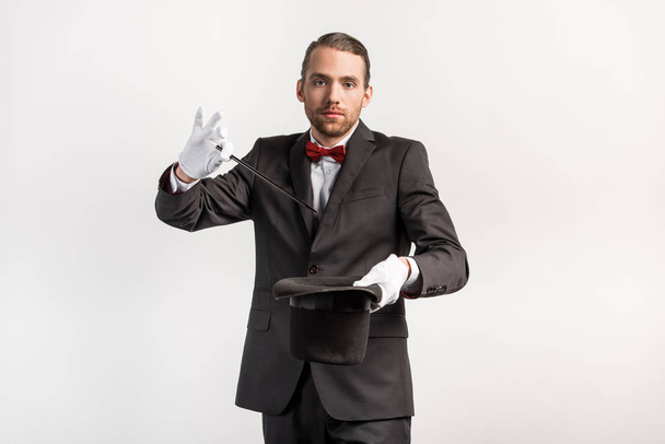 magician in suit making trick hat and wand, isolated on grey - Fotografie, Obrázek