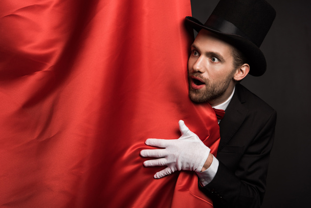 jóképű érzelmi bűvész öltönyben és kalapban cirkuszban vörös függönyökkel - Fotó, kép