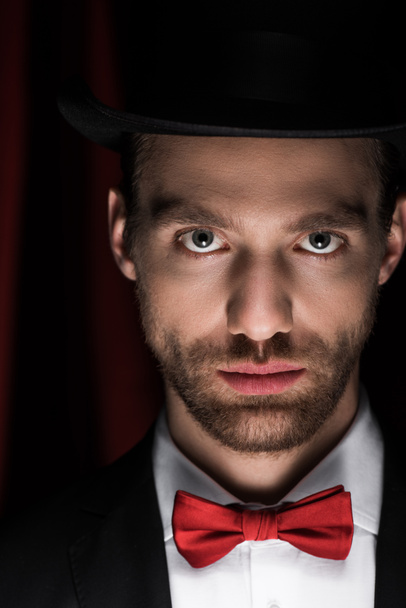 handsome magician in suit, bow tie and hat in circus with red curtains - Foto, immagini
