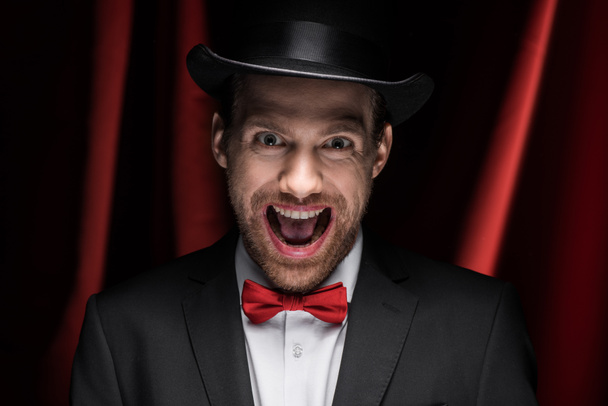 Gruseliger Zauberer mit offenem Mund im Zirkus mit roten Vorhängen - Foto, Bild