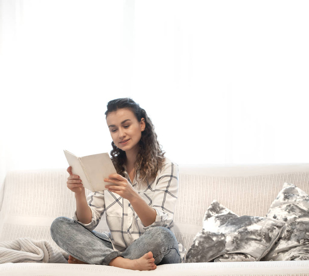 Красивая девушка читает книгу сидя на диване
. - Фото, изображение