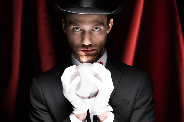 professional magician holding magic ball in circus with red curtains - Photo, image