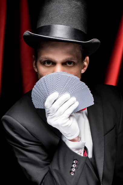 joven mago sosteniendo cartas en circo con cortinas rojas
 - Foto, Imagen