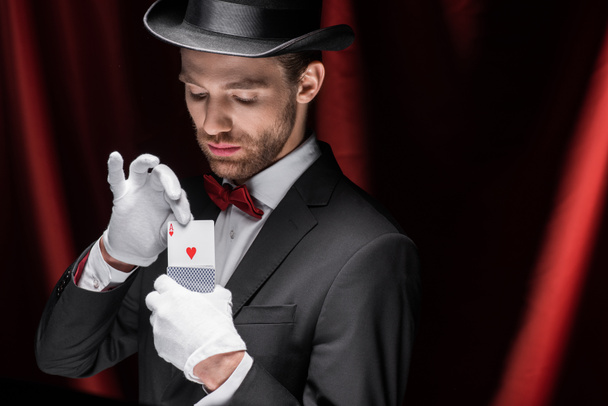 mágico segurando cartas de jogo no circo com cortinas vermelhas
 - Foto, Imagem