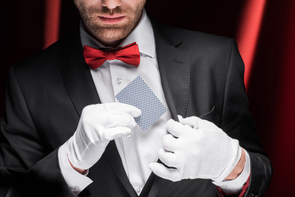 cropped view of magician holding playing card in circus with red curtains - Photo, Image