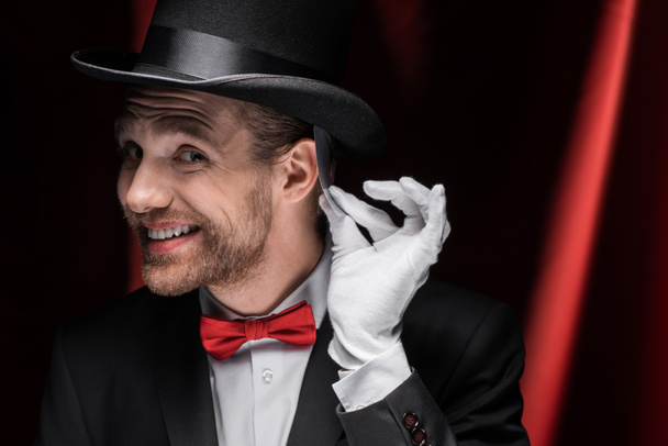 smiling magician holding playing card in circus with red curtains - Foto, immagini