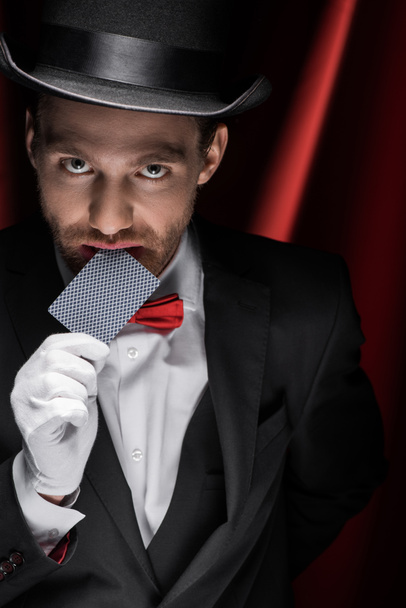 mágico profissional mostrando truque com cartão de jogar no circo com cortinas vermelhas
 - Foto, Imagem