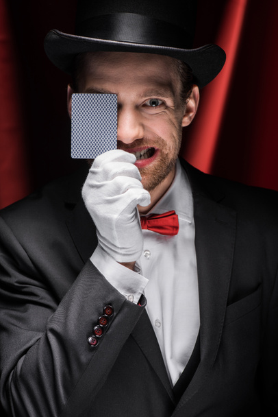 συναισθηματική ταχυδακτυλουργός δείχνει τέχνασμα με το παιχνίδι της κάρτας στο τσίρκο με κόκκινες κουρτίνες - Φωτογραφία, εικόνα