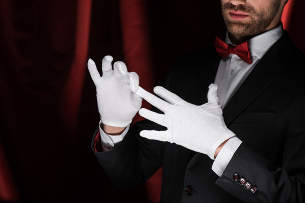 przycięty widok magika zdejmującego białe rękawiczki w cyrku z czerwonymi zasłonami - Zdjęcie, obraz