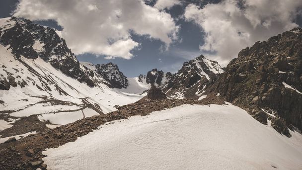 Panorama of the Trans-Ili Alatau mountain range of the Tien Shan system in Kazakhstan near the city of Almaty. Rocky peaks covered with snow and glaciers in the middle of summer under clouds - Foto, Bild
