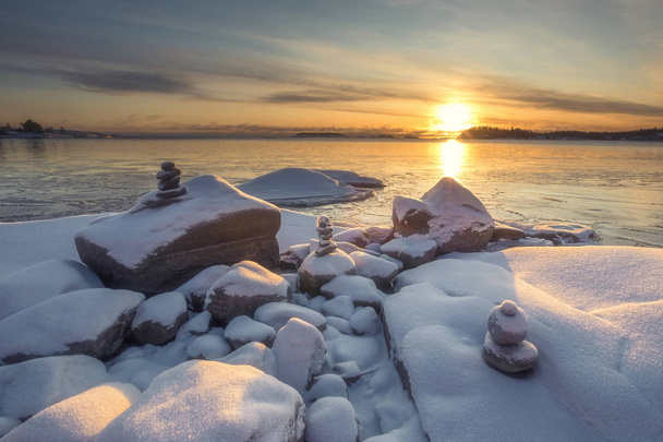 stone pyramids in the snow on the shore of Lake Ladoga in Karelia on a dawn in winter day  - Foto, Imagen