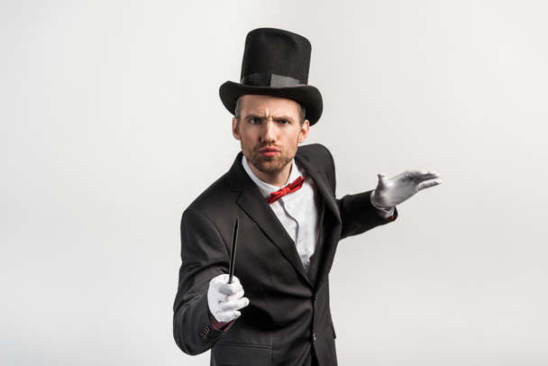 worried magician in suit and hat holding wand, isolated on grey - Fotoğraf, Görsel